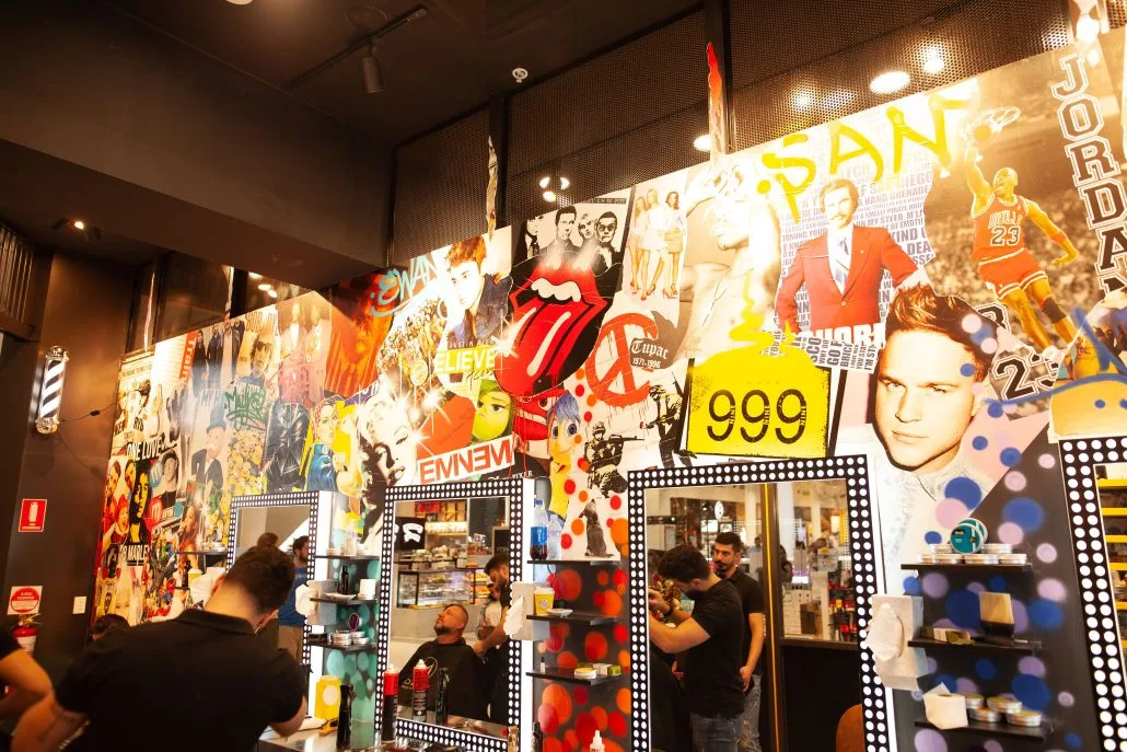 Inside MOE & Co. — a towering poster wall: Rolling Stones, Eminem, Tupac, barber pole and bulb-framed mirrors