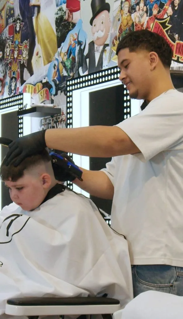A young boy in a white cape getting a clipper cut against the poster wall — the first-trim end of the room