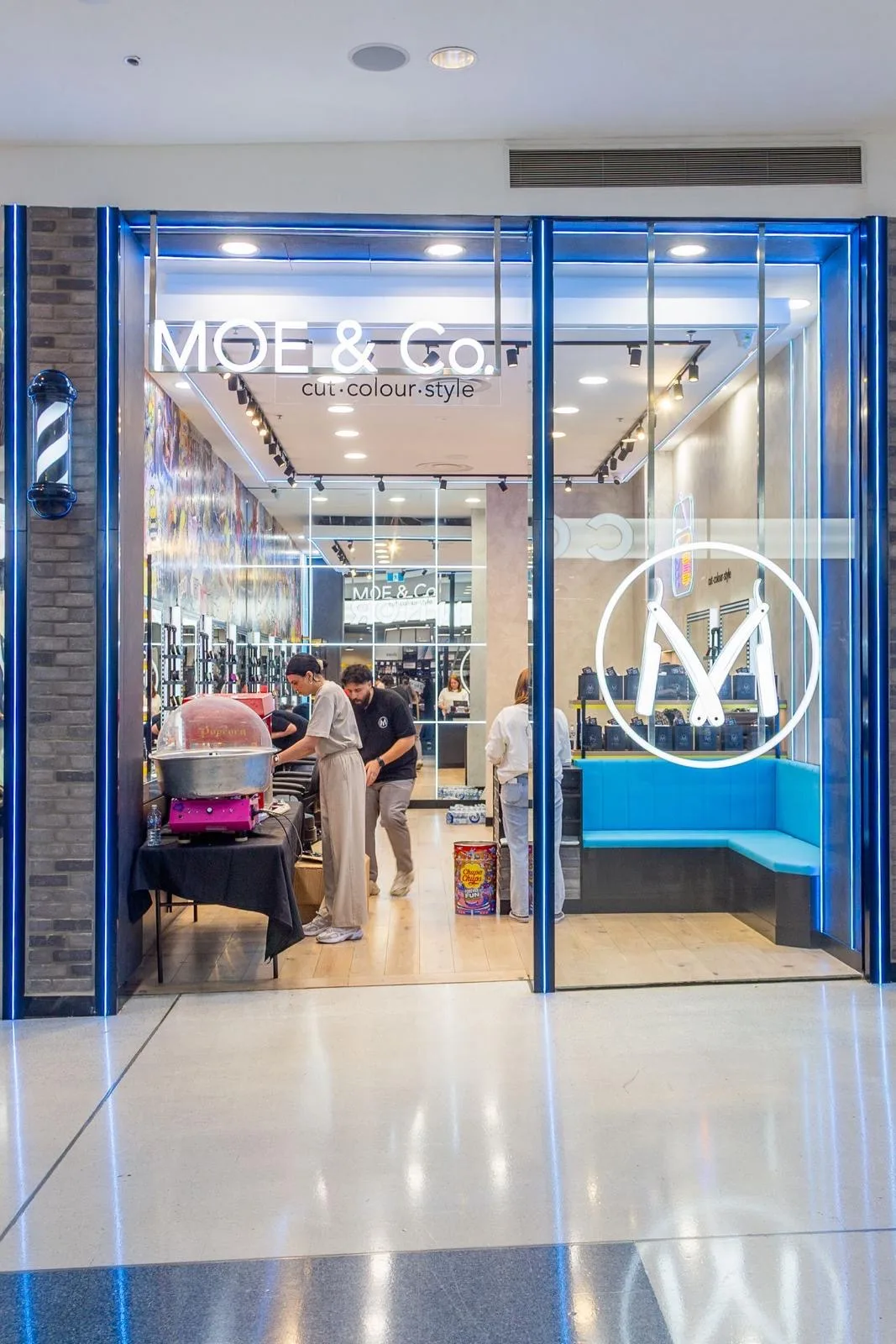 A MOE & Co. shopfront at night — cut·colour·style on the glass, blue neon, chrome barber pole