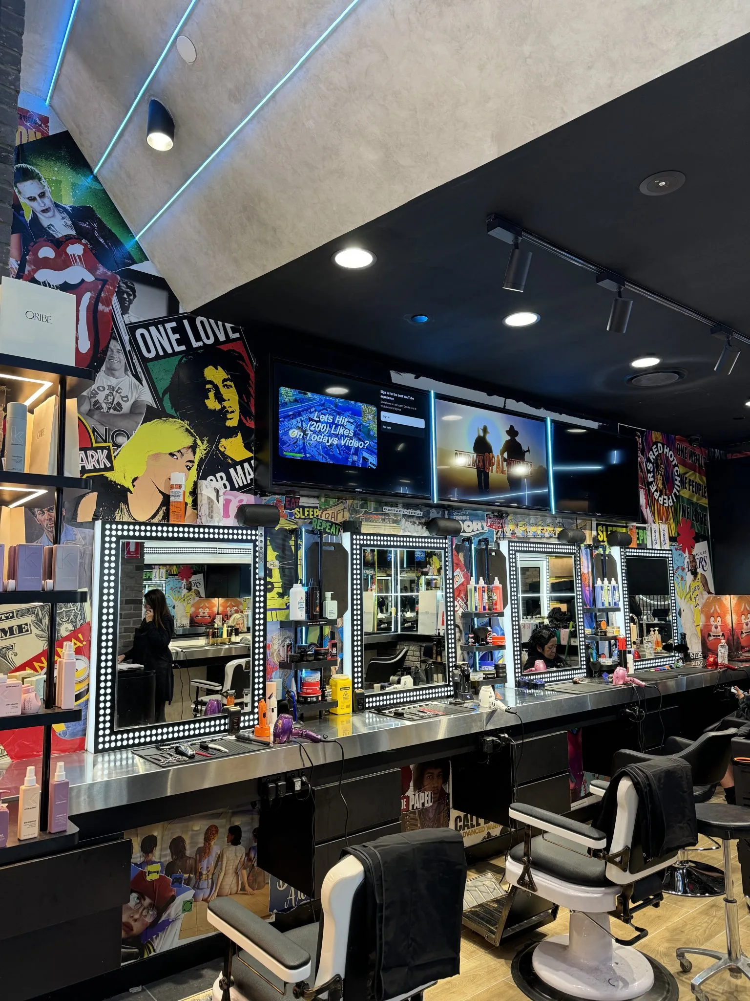 Inside MOE & Co. — blue neon ceiling strips, the poster wall and bulb-framed mirror stations